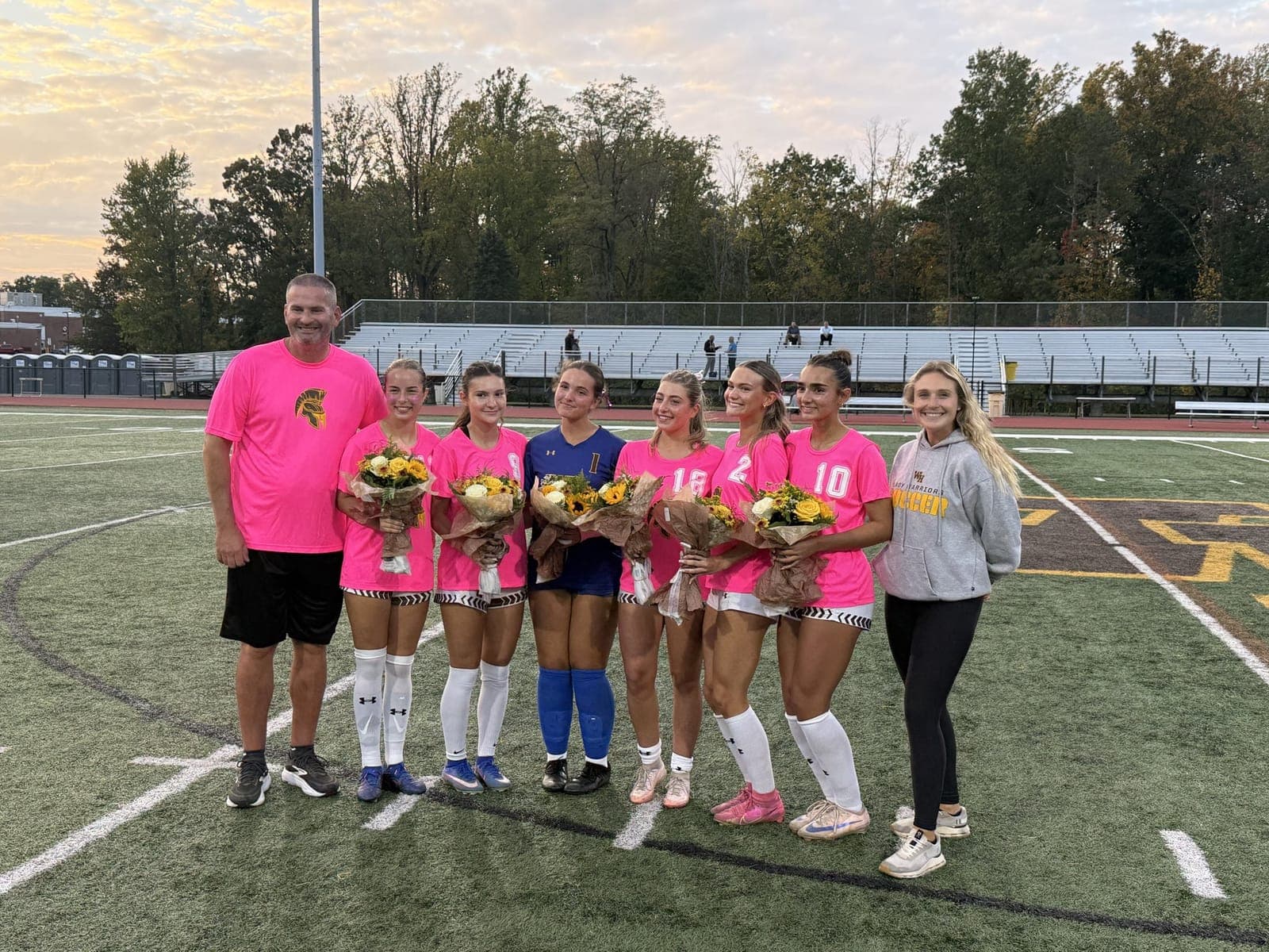 Watchung Hills girls soccer seniors and coaches gather on the field with flowers.